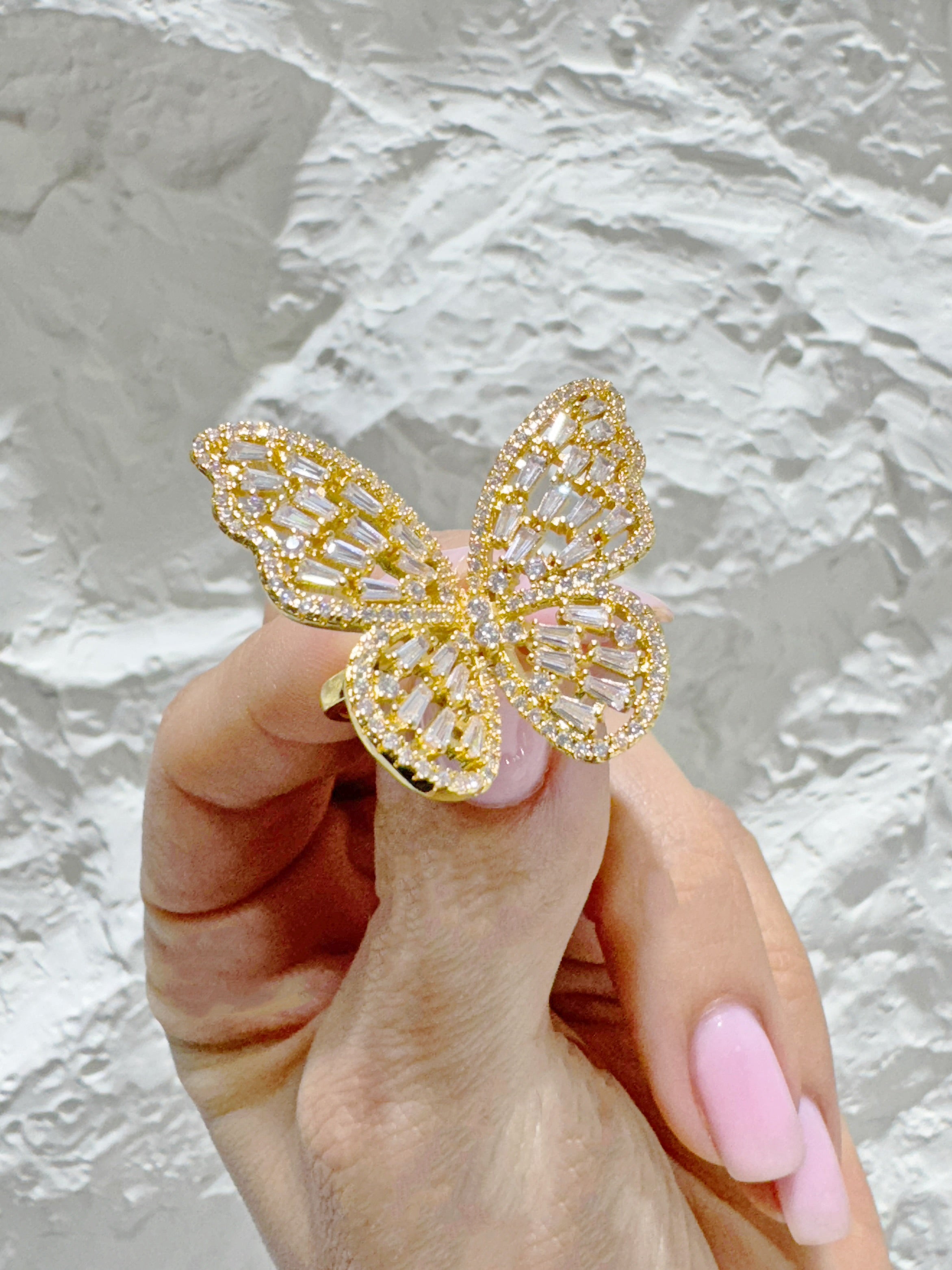 Gold butterfly ring held by a hand with pink nail polish