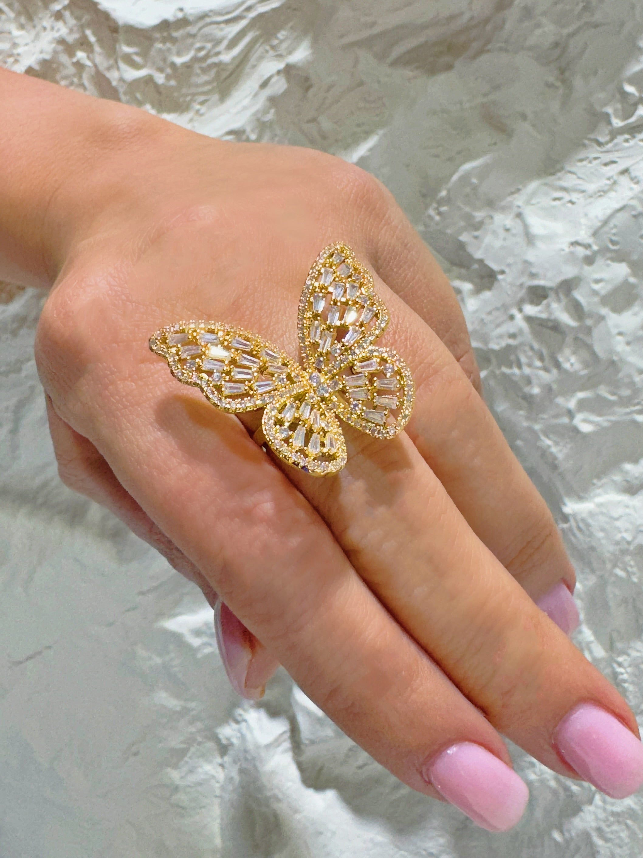 Gold butterfly ring on a hand with pink nail polish